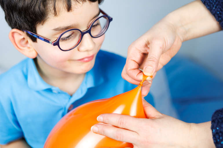 Le petit garçon regarde un adulte faire un noeud pour fermer le ballon.